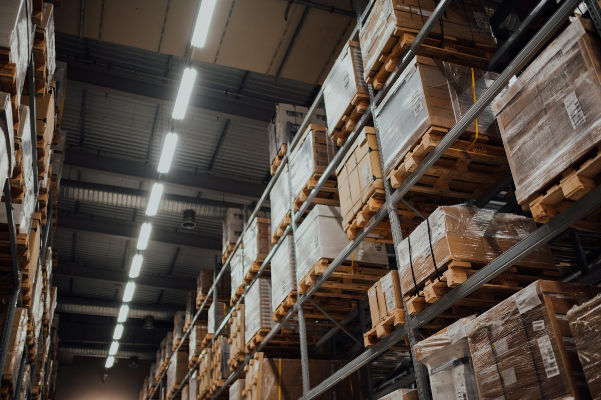 Tall metal racks packed with wrapped boxes on wooden pallets under strip lights